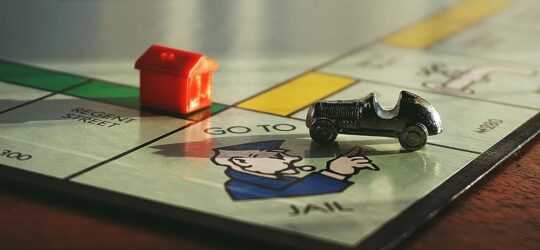 Close up of a monopoly board at the corner where it says Got to Jail and there is a car piece as well as a red house on the board.
