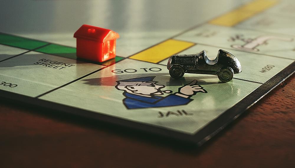 Close up of a monopoly board at the corner where it says Got to Jail and there is a car piece as well as a red house on the board.
