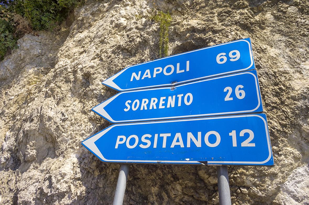 three stacked blue signs that say Napoli 69, Sorrento 26, Positano 12.