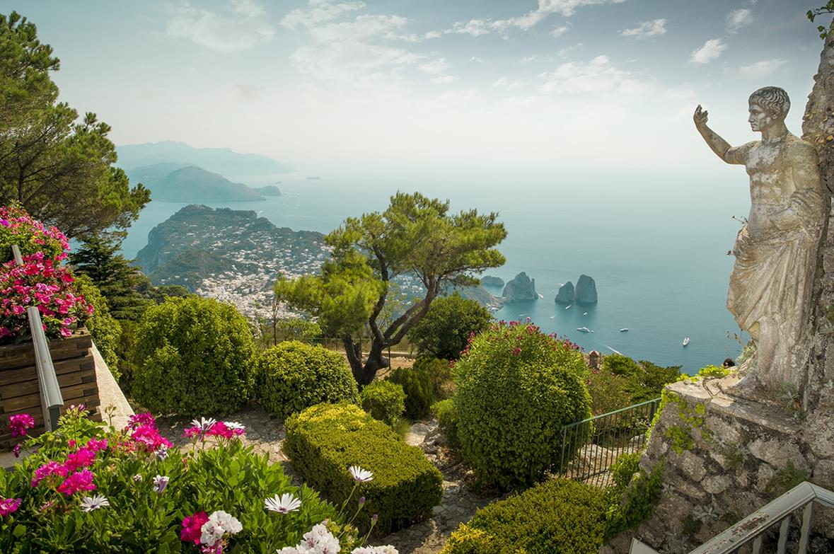 View of the Amalfi Coast from the top of a mountain with green bushes and a roman statue in front of us.