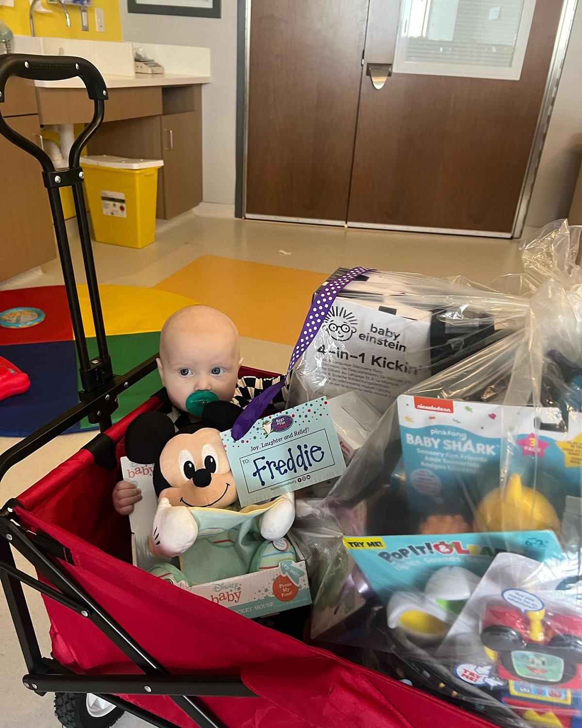 Baby Freddie in a red wagon with all of his toys around him