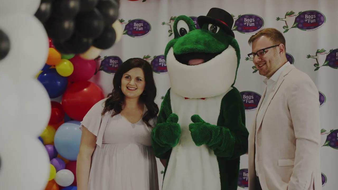 Two people posing with Chuckles the frog mascot