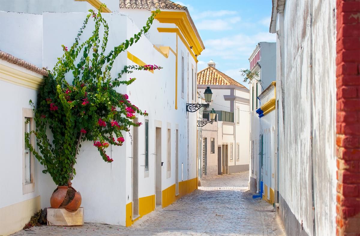 A narrow Portugal city street with white two story buildings on either side.