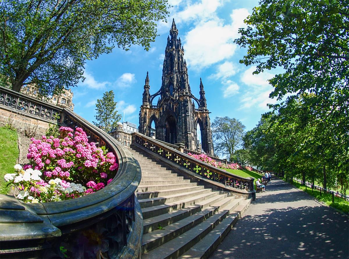 Stairs with flowers and trees around it and a large castle in the background. It is a beautiful sunny day outside.