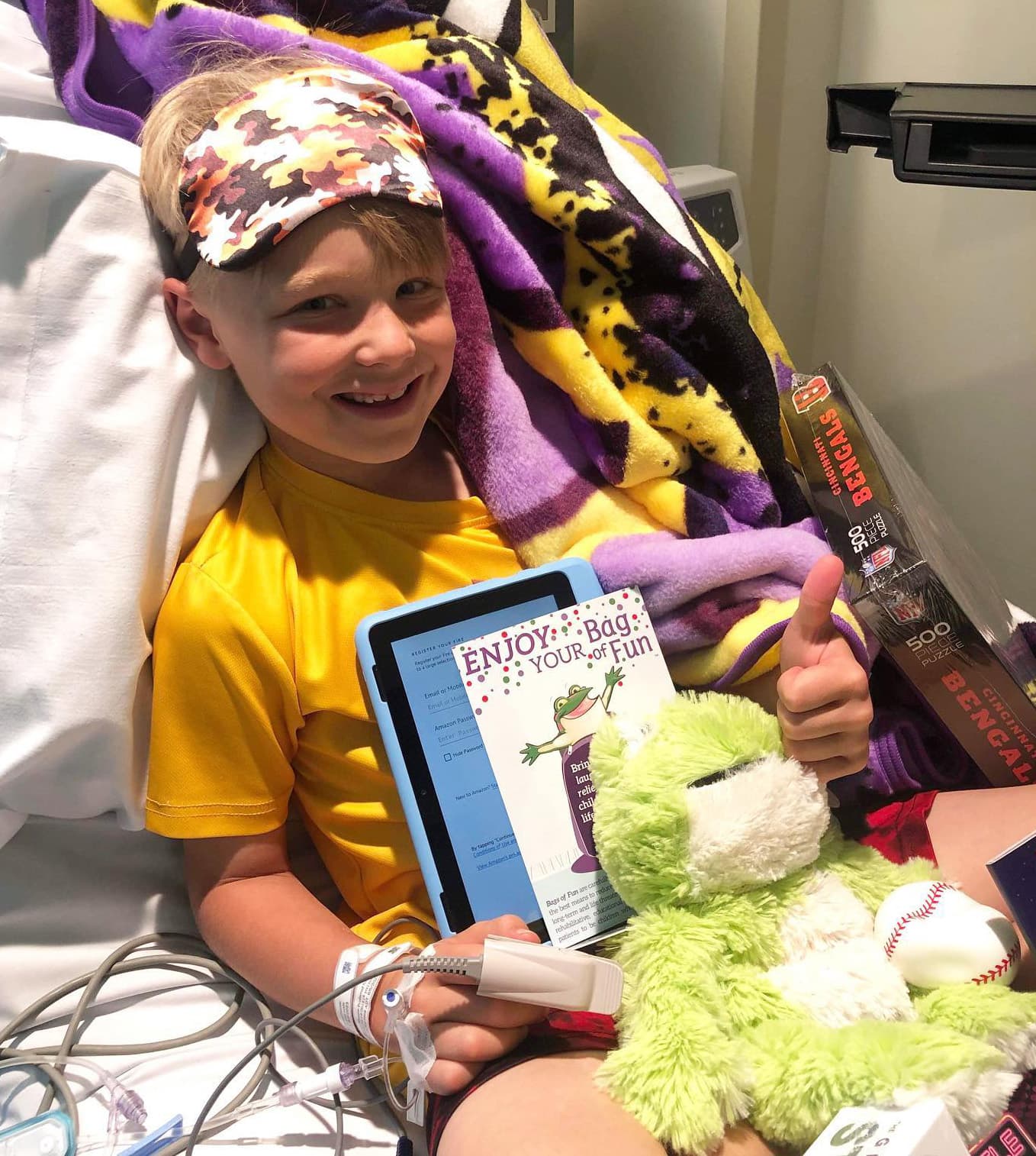 Boy in a hospital bed with a bags of fun card and toys and comfort items around him.