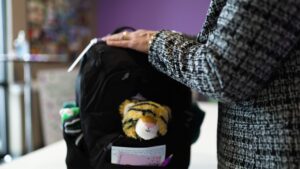 a close up of an arm on a black backpack that has a stuffed tiger sticking out from a pocket.