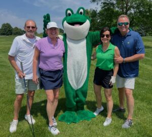 Four people on the golf course with the frog mascot.