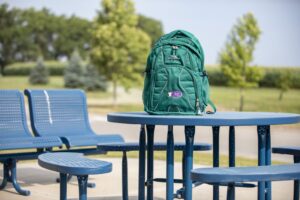 Turquoise backpack sitting on a picnic bench with trees behind it in the distance