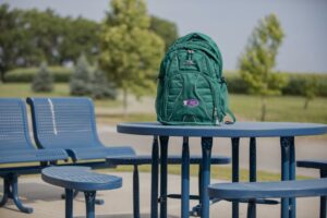 Turquoise backpack sitting on a picnic bench with trees behind it in the distance