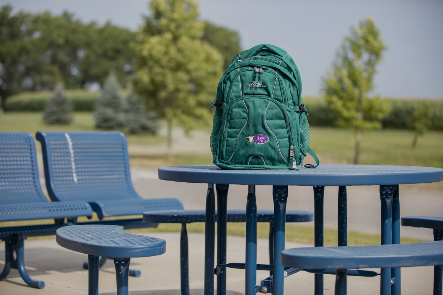 Turquoise backpack sitting on a picnic bench with trees behind it in the distance