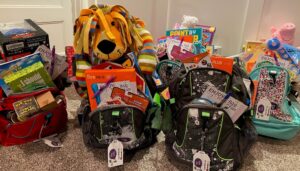 A group of backpacks stuffed with games, toys, and stuffed animals set down on the carpet.
